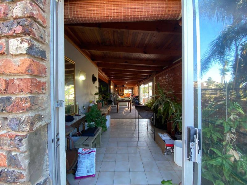 A covered patio area featuring exposed timber beam ceilings, tiled flooring, and sliding glass door access, providing a versatile outdoor entertainment space.