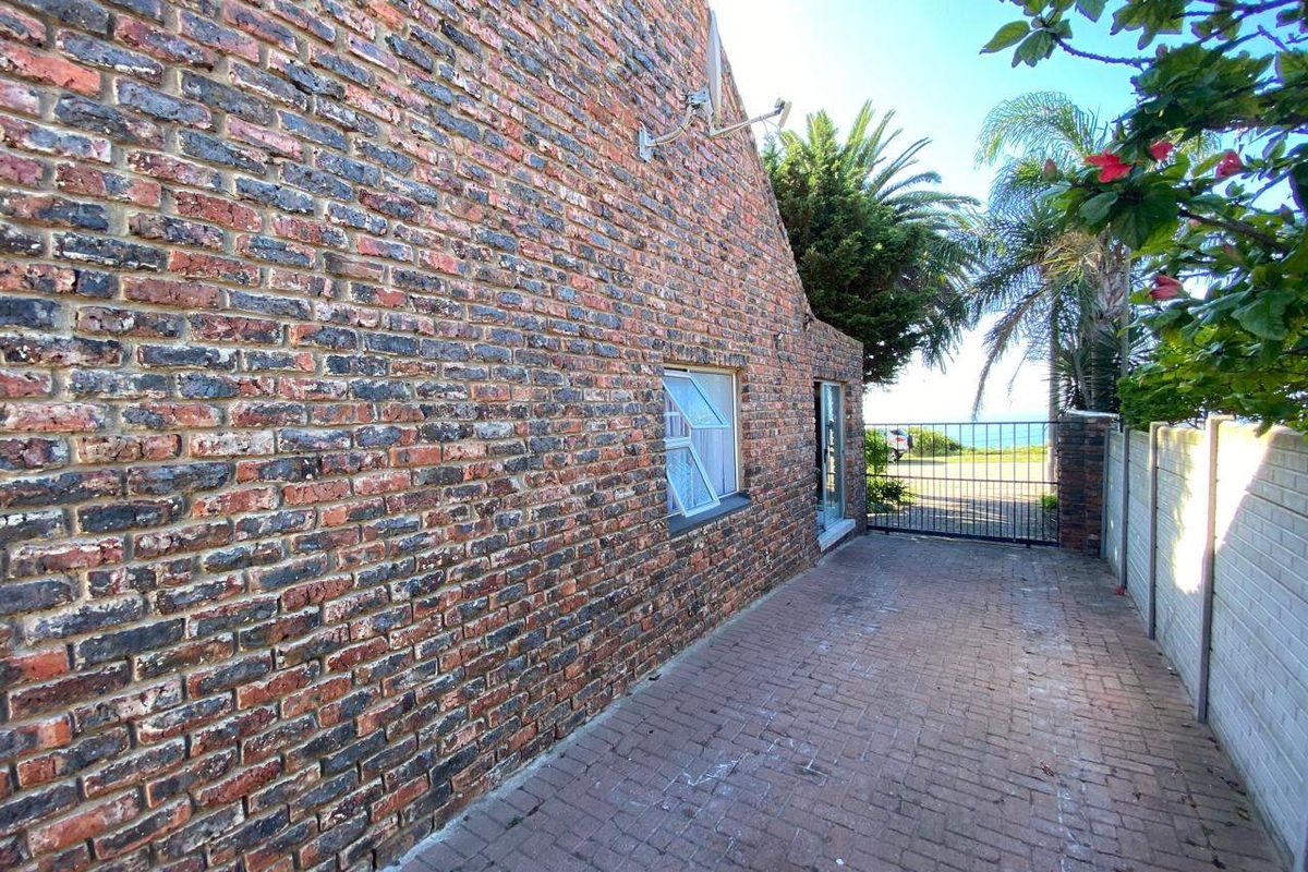 A side view of the property featuring a face brick exterior, paved driveway, and secure metal gate leading towards the rear area.