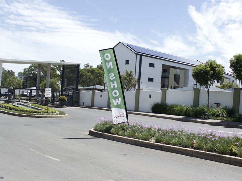 The entrance to Green Park apartment complex featuring a modern security gatehouse, perimeter wall with electric fencing, and solar-equipped residential buildings.