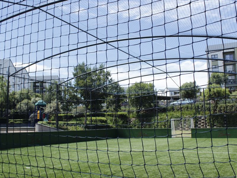A well-maintained outdoor sports facility featuring artificial turf, perimeter netting, and a soccer goal, situated within an apartment complex.