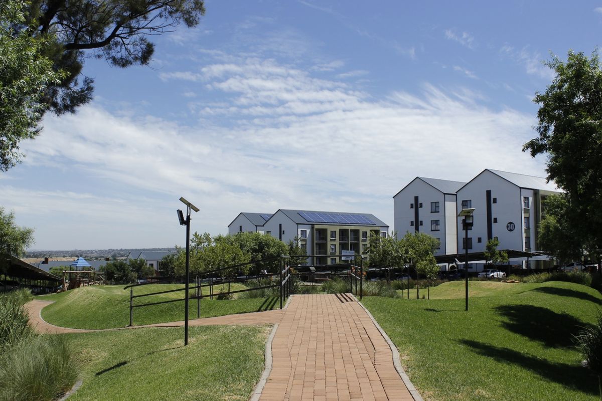 A view of the apartment complex grounds featuring landscaped gardens, paved walkways, solar lighting, and multi-story residential buildings with rooftop solar panels.