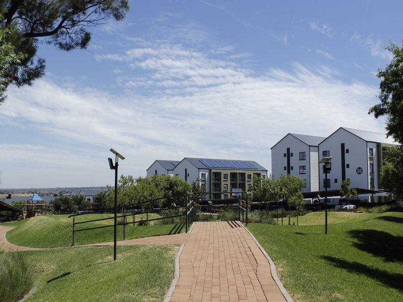 A view of the apartment complex grounds featuring landscaped gardens, paved walkways, solar lighting, and multi-story residential buildings with rooftop solar panels.