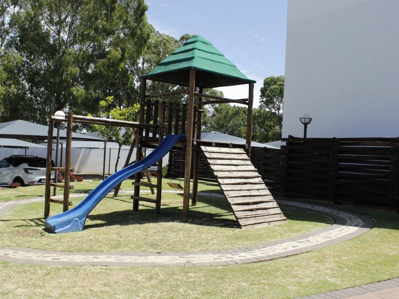 Communal garden area featuring a children's playground structure, timber fencing, and paved pathways within the apartment complex grounds.