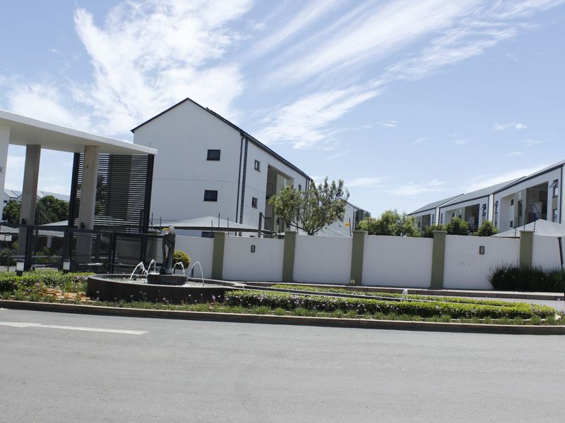 The entrance to Green Park apartment complex featuring a modern security gatehouse, perimeter wall with electric fencing, and a landscaped water fountain feature.