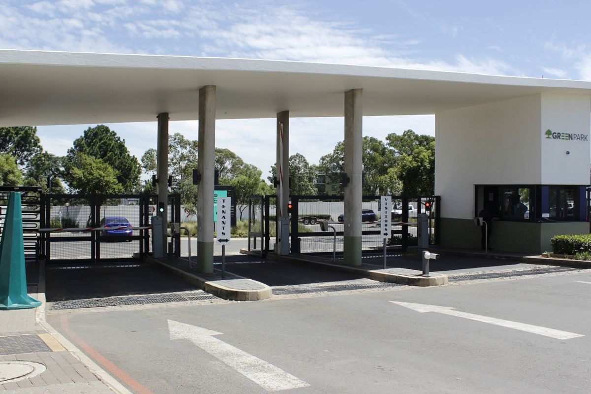 The main entrance and security gatehouse of the Green Park apartment complex, featuring controlled access boom gates and a modern structural canopy.