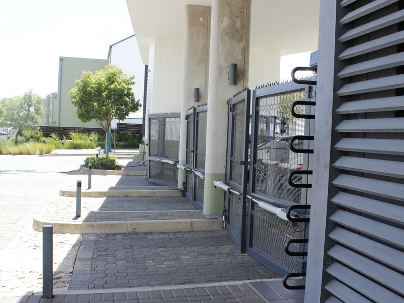 Modern apartment complex entrance featuring a secure gated access point, paved driveway, and architectural concrete columns.