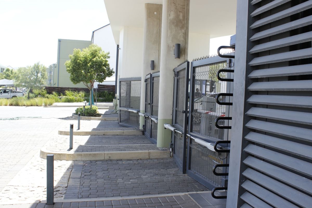 Modern apartment complex entrance featuring a secure gated access point, paved driveway, and architectural concrete columns.