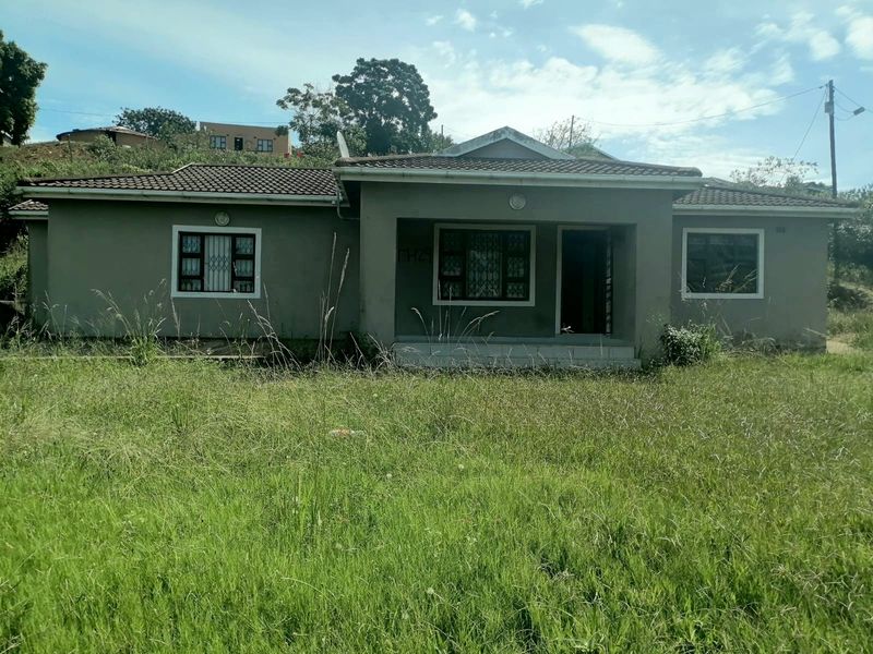 Front elevation of a single-story house featuring a tiled roof, security bars on windows, and a covered entrance porch, set on an overgrown lot.