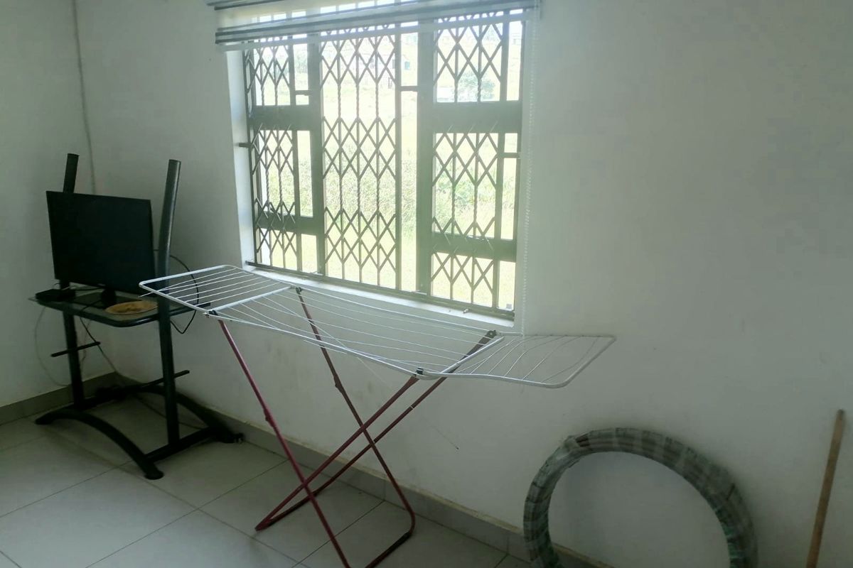 A simple living area featuring tiled flooring and a window fitted with a security gate and blinds.