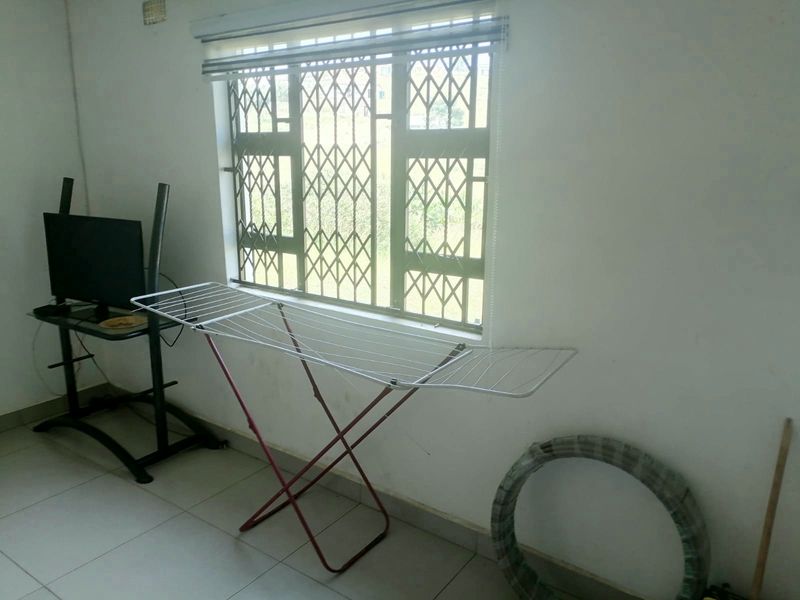 A simple living area featuring tiled flooring and a window fitted with a security gate and blinds.