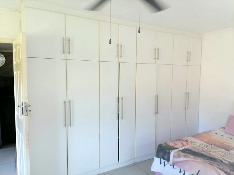 A bedroom featuring extensive floor-to-ceiling built-in cupboards with modern handles and a ceiling fan.