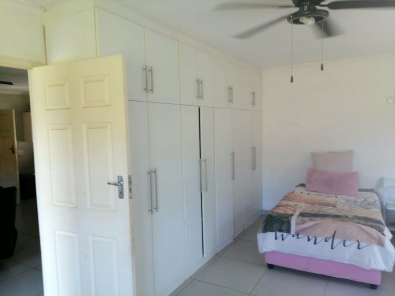 A bedroom featuring white built-in cupboards, a ceiling fan, and tiled flooring.