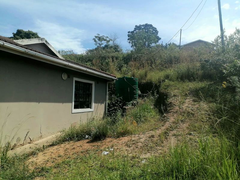 Rear exterior view of the property showing a water storage tank, overgrown garden area, and visible cracks in the exterior wall plaster.