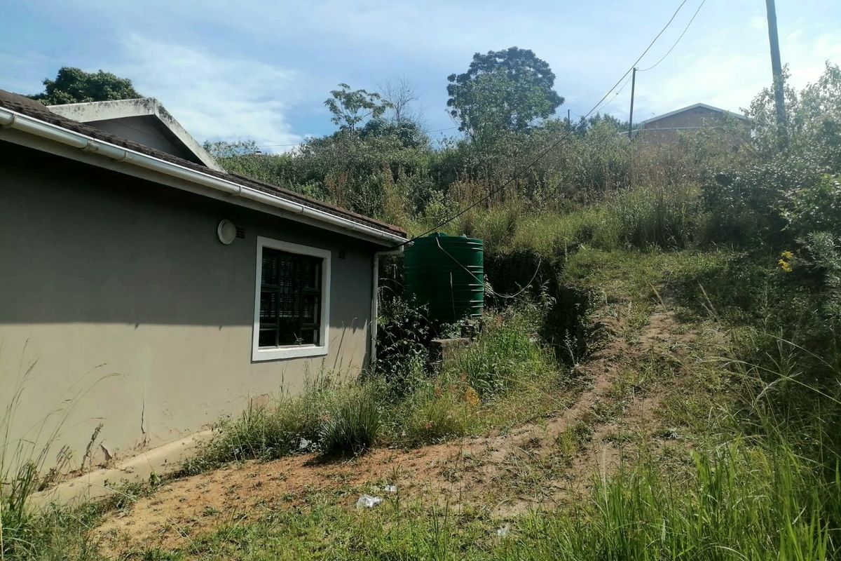 Rear exterior view of the property showing a water storage tank, overgrown garden area, and visible cracks in the exterior wall plaster.