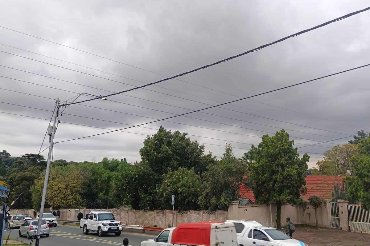 A street-level view showing the neighbourhood approach, including utility infrastructure, boundary walls, and surrounding greenery under an overcast sky.