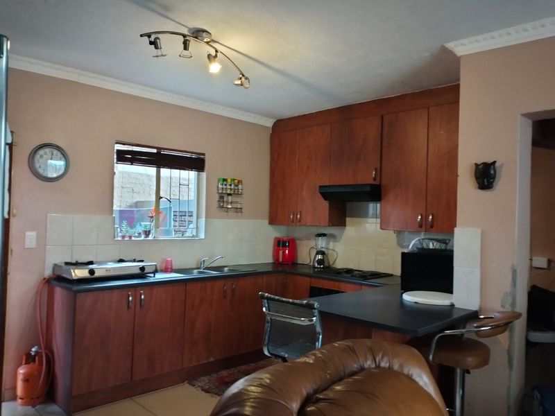Functional kitchen featuring wooden cabinetry, laminate countertops, gas hob, and tiled backsplash, with some minor wall finish repairs required near the entrance.