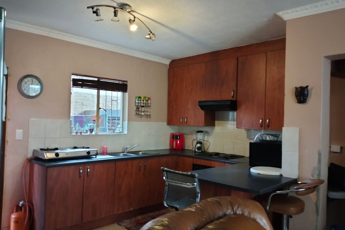 Functional kitchen featuring wooden cabinetry, laminate countertops, gas hob, and tiled backsplash, with some minor wall finish repairs required near the entrance.