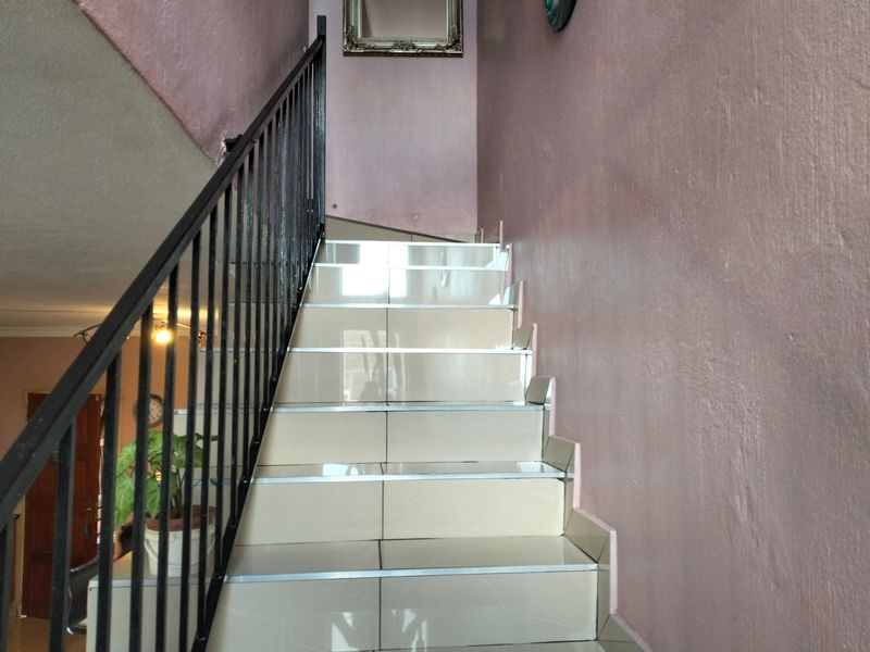 A staircase featuring tiled treads and a black metal balustrade, leading to an upper level within the townhouse.