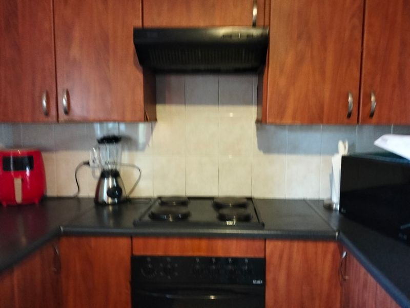 A functional kitchen featuring wood-look cabinetry, a built-in oven, electric hob, and a tiled splashback.