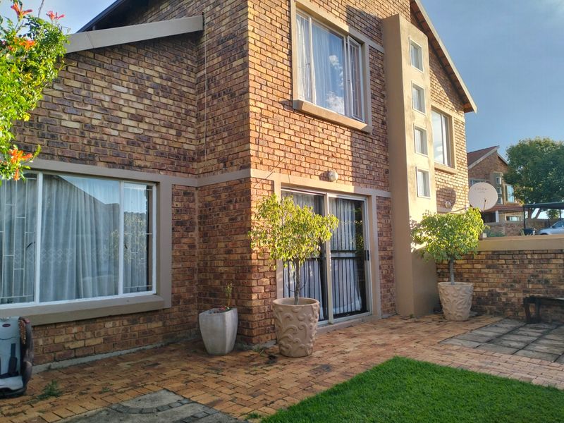 Rear exterior view of a face brick townhouse featuring a paved patio area and sliding glass door access to the interior.