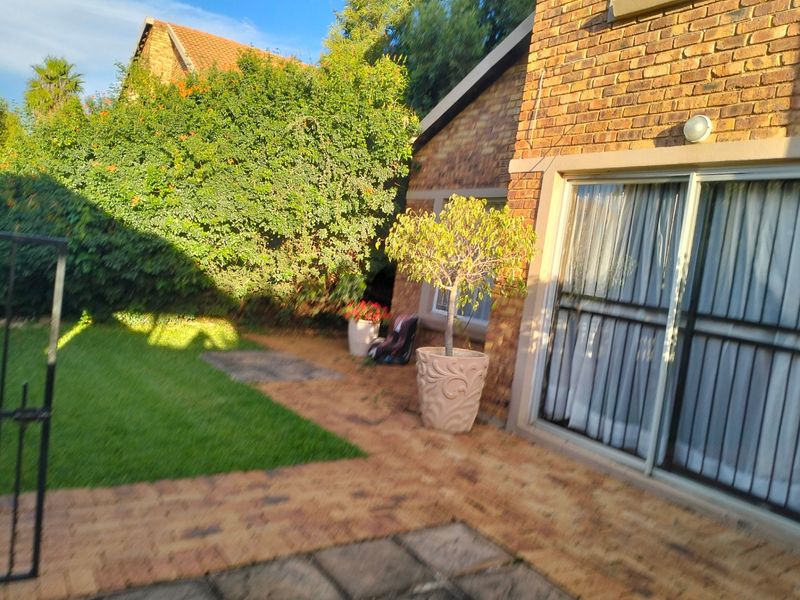 A rear exterior view of the townhouse featuring a brick facade, paved patio area, and a small private lawn.