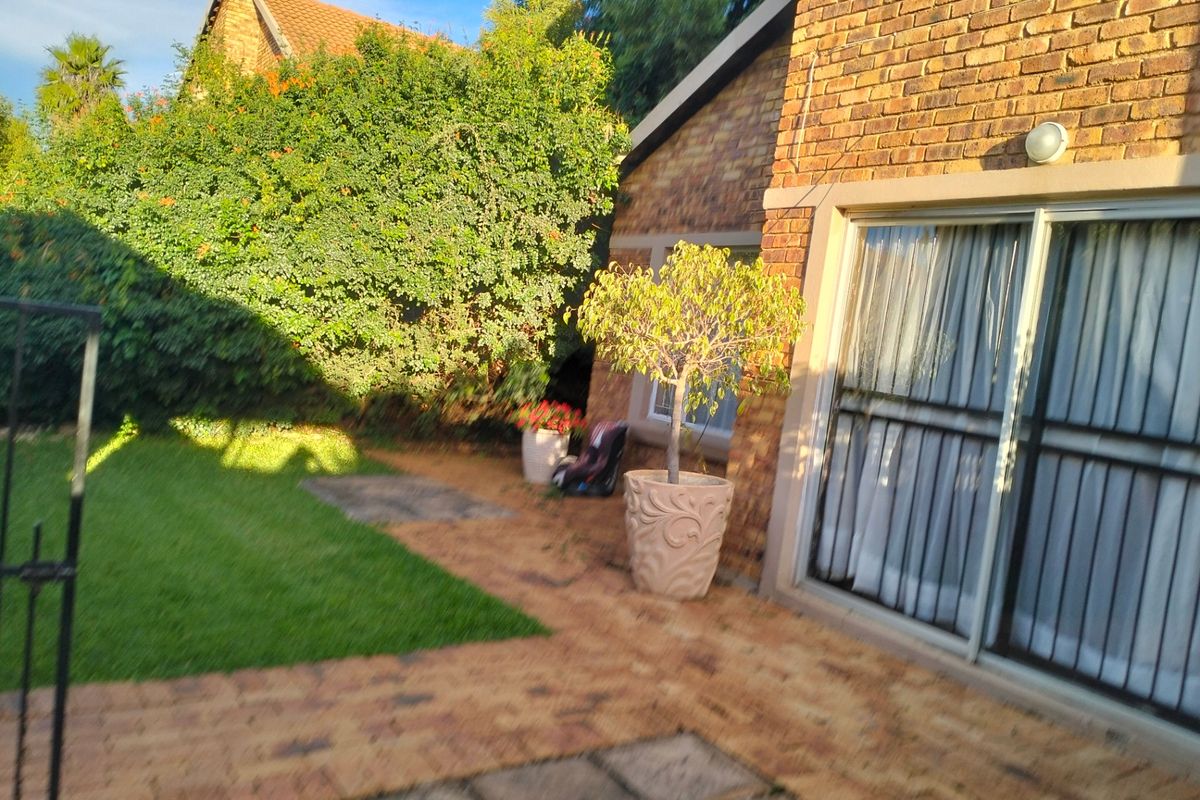 A rear exterior view of the townhouse featuring a brick facade, paved patio area, and a small private lawn.