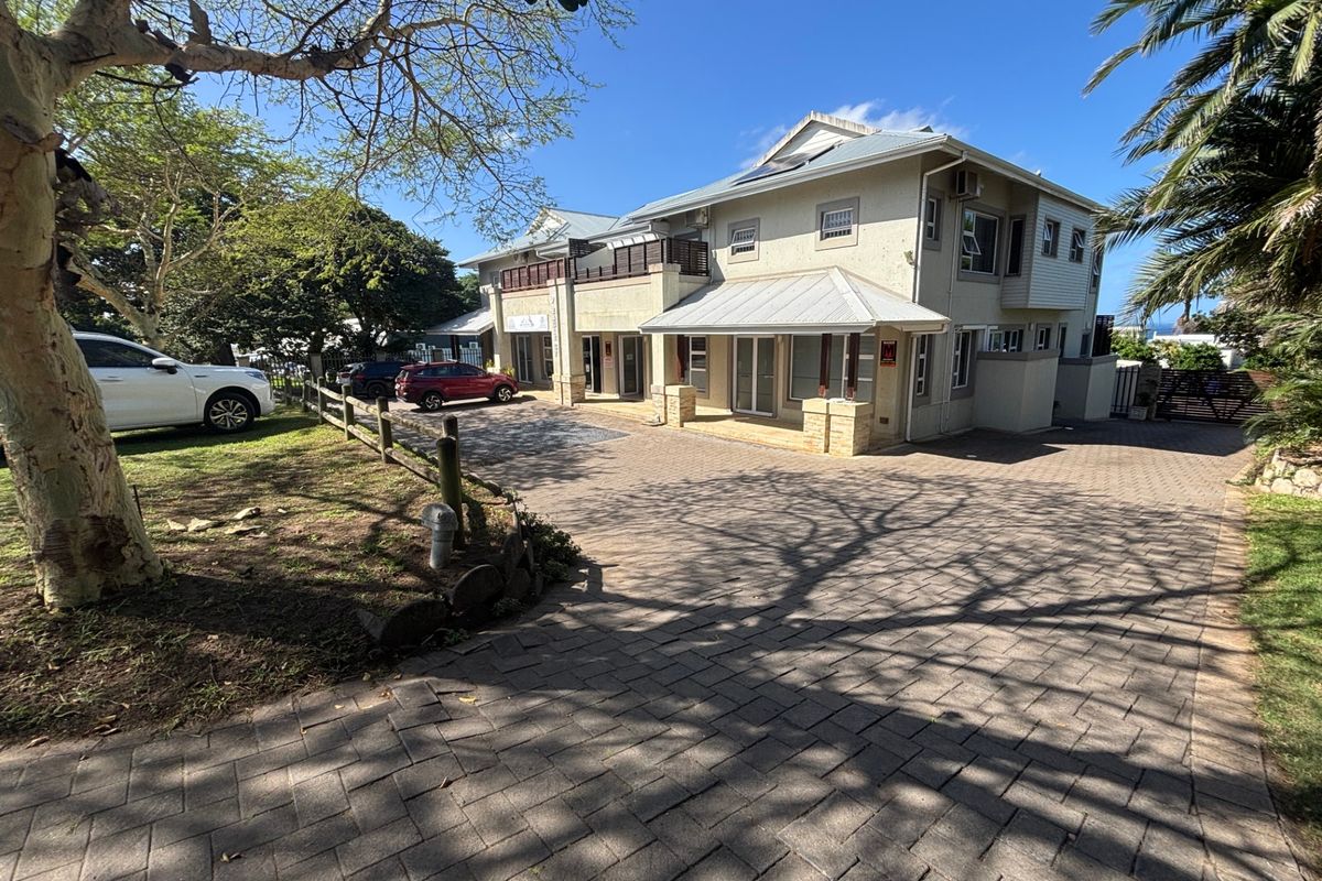 Front elevation of a multi-story commercial property featuring a paved driveway, metal roofing, and a balcony with timber railings.