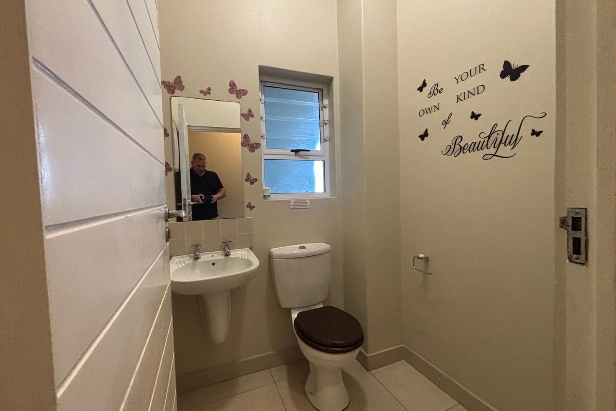 A functional guest bathroom featuring a pedestal sink, dual-flush toilet, and tiled flooring with a louvered window for ventilation.