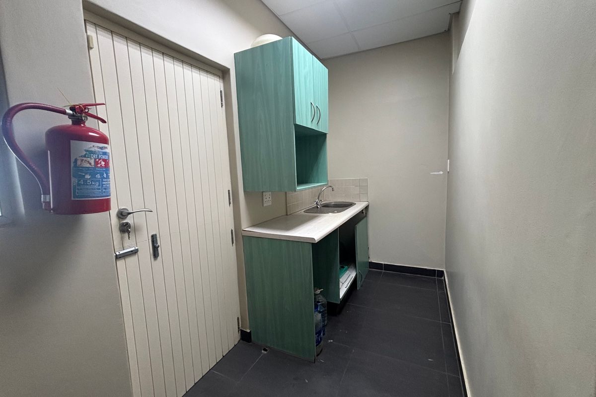 A functional kitchenette area featuring built-in cabinetry, a stainless steel sink, and tiled flooring, suitable for office or commercial utility use.