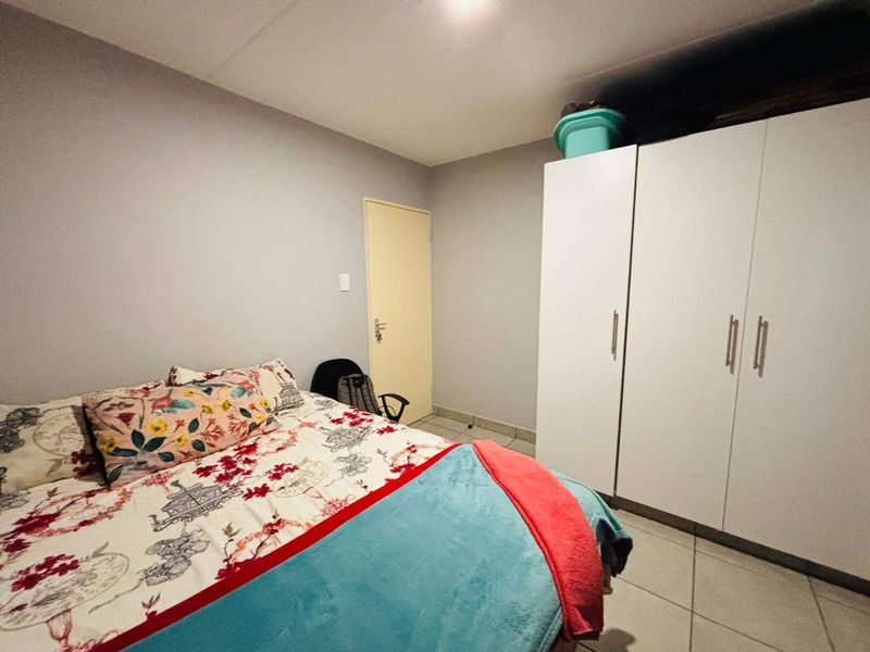 A bedroom featuring tiled flooring and a white built-in wardrobe, providing functional storage space within the apartment.