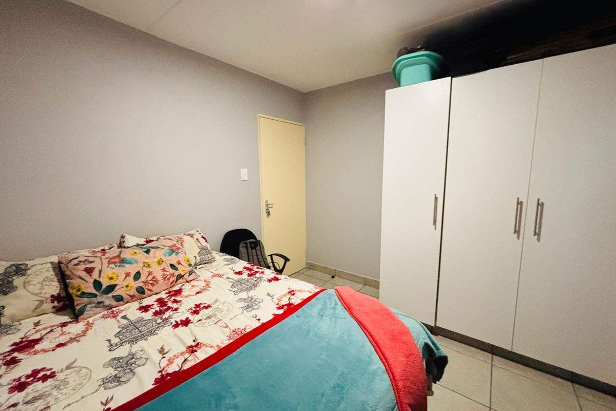 A bedroom featuring tiled flooring and a white built-in wardrobe, providing functional storage space within the apartment.