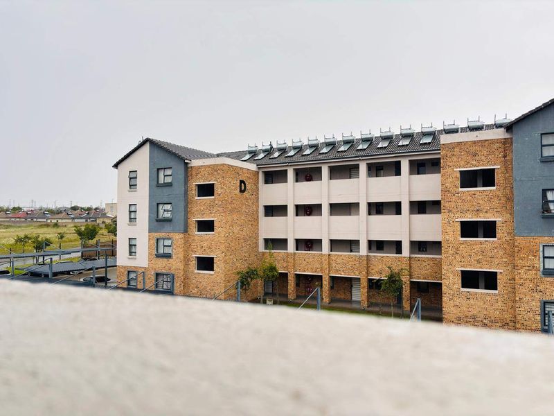 Exterior view of a multi-story apartment building featuring face brick construction, solar water heating panels, and covered parking facilities.
