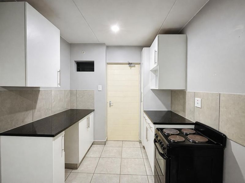 A clean, functional kitchen featuring white cabinetry, dark stone countertops, tiled backsplash, and a freestanding electric stove.