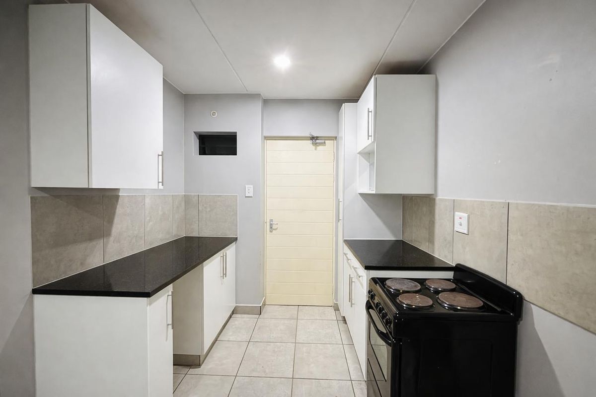 A clean, functional kitchen featuring white cabinetry, dark stone countertops, tiled backsplash, and a freestanding electric stove.