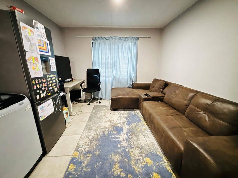 An open-plan living area featuring tiled flooring and a window with a curtain rod, providing a functional space for relaxation and daily activities.