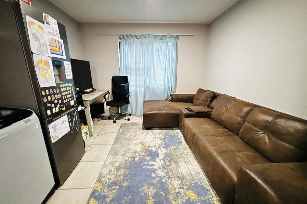 An open-plan living area featuring tiled flooring and a window with a curtain rod, providing a functional space for relaxation and daily activities.