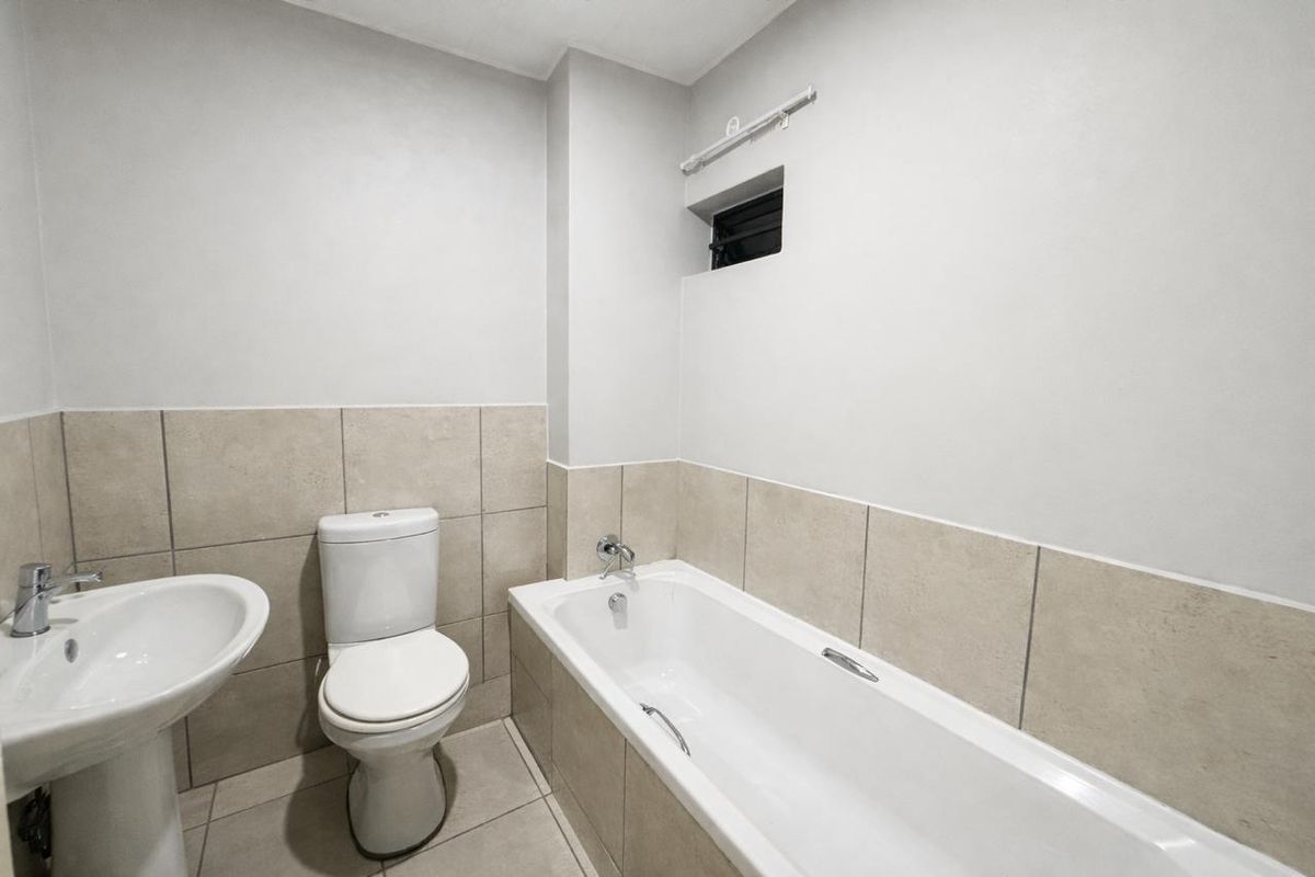 A clean, modern bathroom featuring a white pedestal basin, toilet, and bathtub with neutral ceramic tiling throughout.