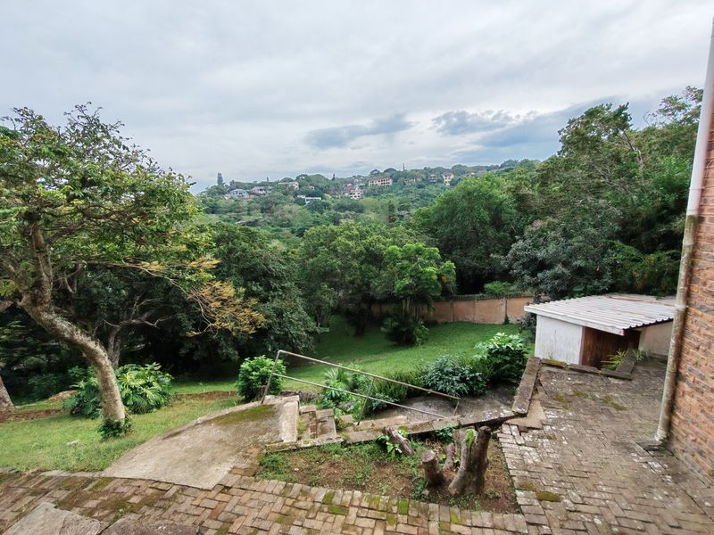 Rear view of the property featuring a brick paved patio, concrete stairs with metal handrail, and a small storage shed overlooking a lush garden.