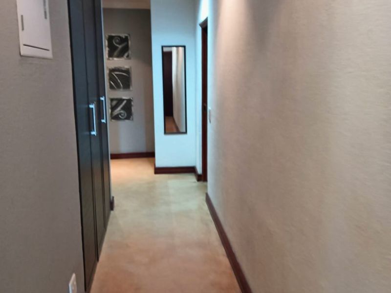 A clean and well-lit hallway featuring tiled flooring, recessed downlights, and built-in storage cupboards.