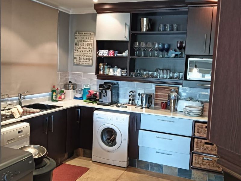 A functional kitchen featuring dark and light cabinetry, integrated laundry appliances, tiled backsplash, and ample storage space with a neutral aesthetic.