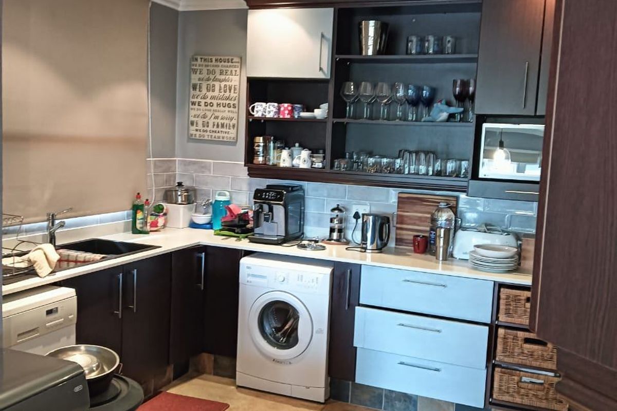 A functional kitchen featuring dark and light cabinetry, integrated laundry appliances, tiled backsplash, and ample storage space with a neutral aesthetic.
