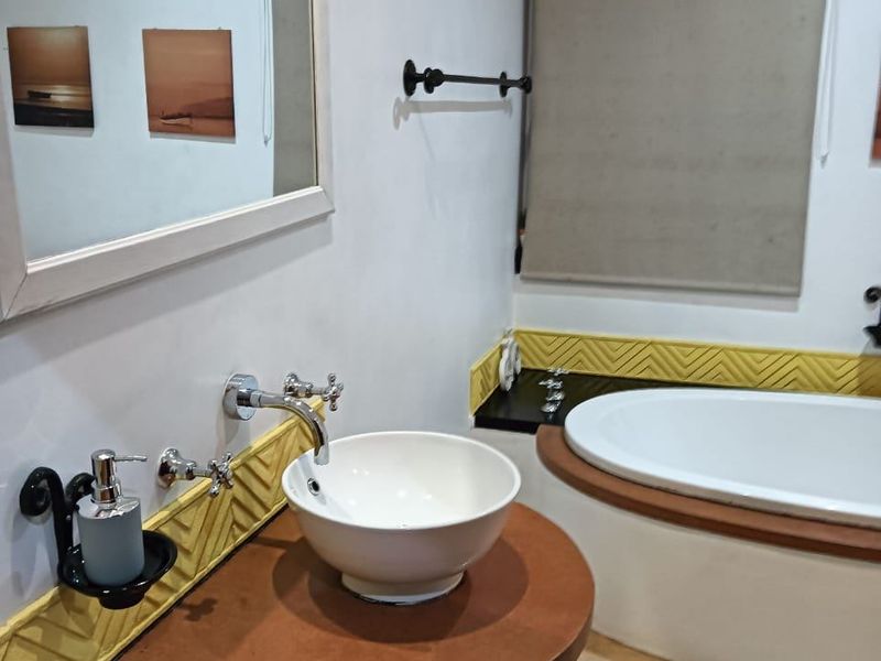 A well-maintained bathroom featuring a modern vessel sink, wall-mounted chrome faucet, and a built-in bathtub with decorative yellow tiled accents.