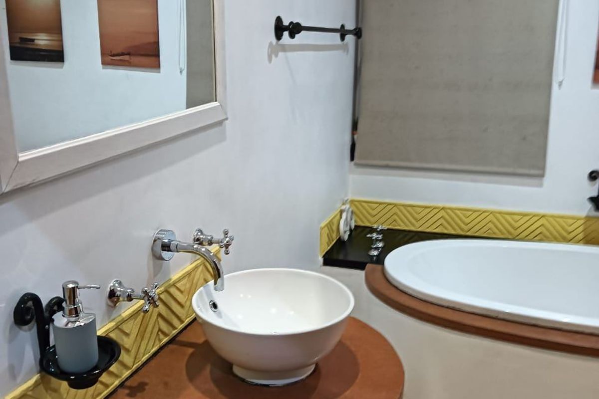 A well-maintained bathroom featuring a modern vessel sink, wall-mounted chrome faucet, and a built-in bathtub with decorative yellow tiled accents.
