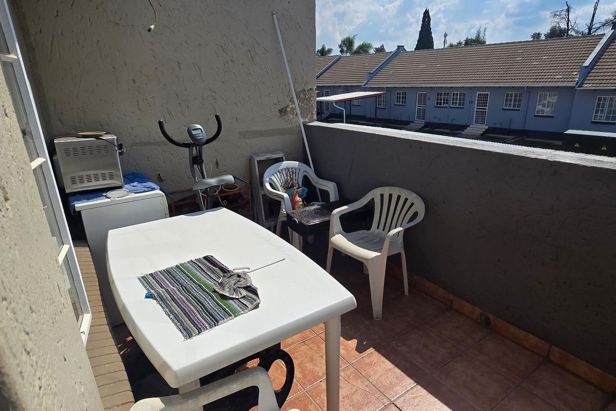 An outdoor balcony area featuring tiled flooring and a concrete balustrade, showing signs of wear on the wall surfaces.