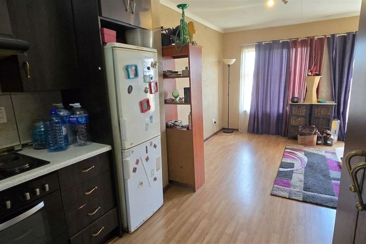Open-plan kitchen and living area featuring dark cabinetry, laminate flooring, and an integrated electric hob and oven setup.
