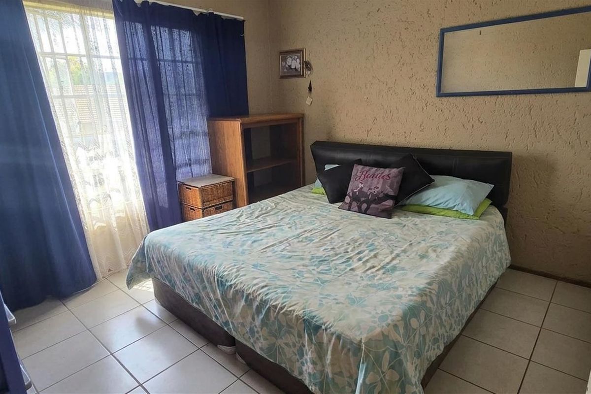 A functional bedroom featuring tiled flooring, textured walls, and a sliding glass door providing natural light.
