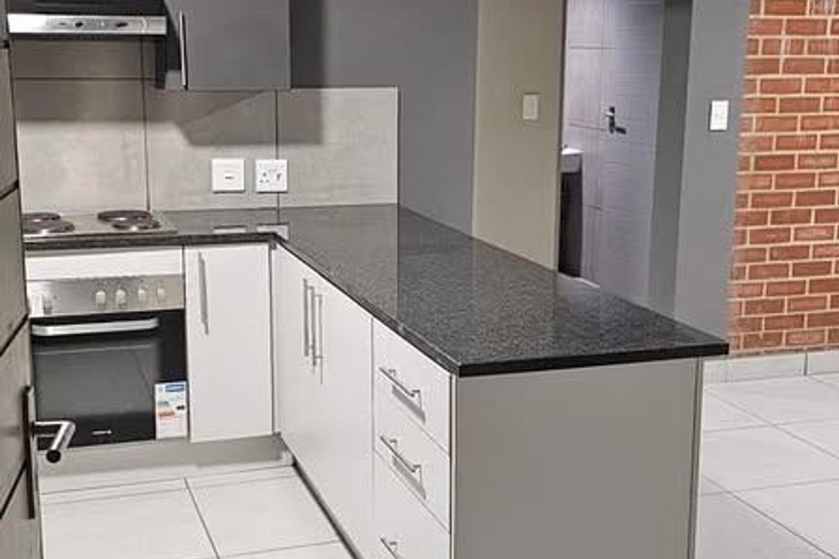 Modern kitchen featuring sleek white and grey cabinetry, granite countertops, built-in oven, hob, extractor fan, and stylish exposed brick and concrete architectural elements.