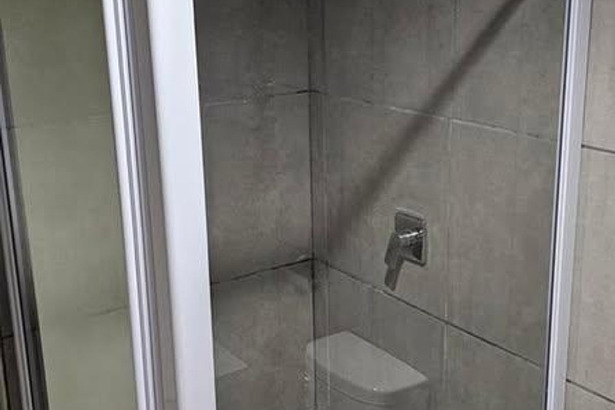A compact bathroom shower enclosure featuring grey wall tiles, a white frame, and standard plumbing fixtures.