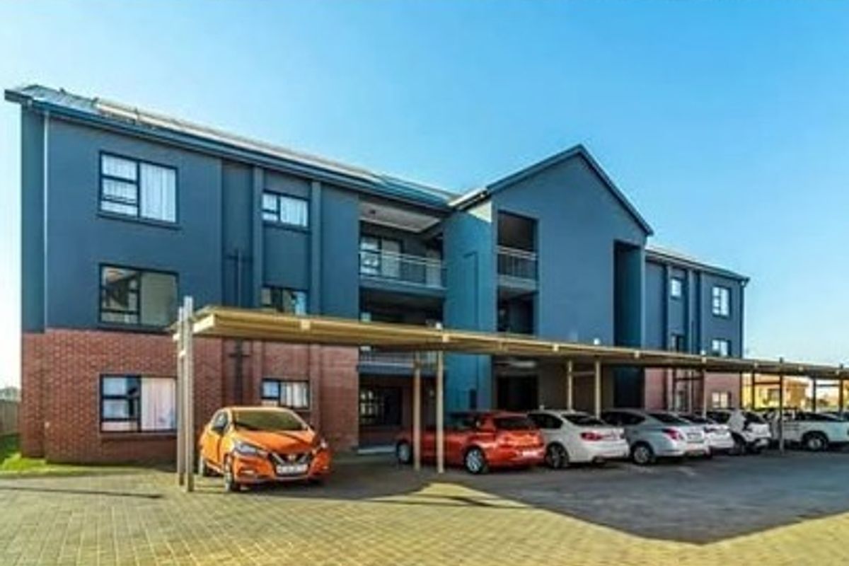 Front elevation of a multi-story apartment complex featuring a brick and painted plaster facade with covered parking bays and balconies.