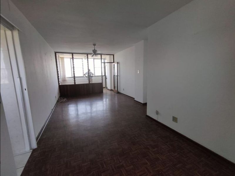 An empty, open-plan living area featuring original parquet flooring, large windows with a view, and a ceiling fan.